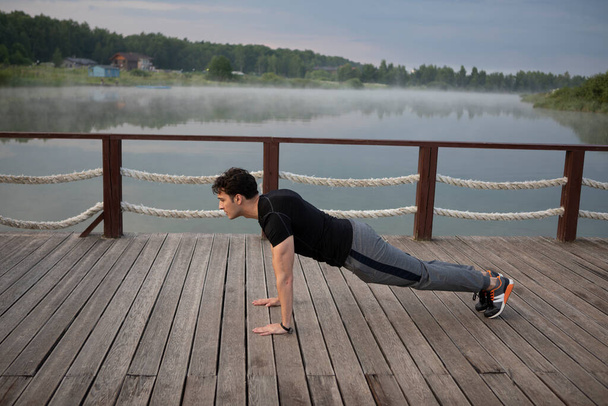 Young sporty man training on nature. Push up and plank close to the foggy lake - Photo, Image