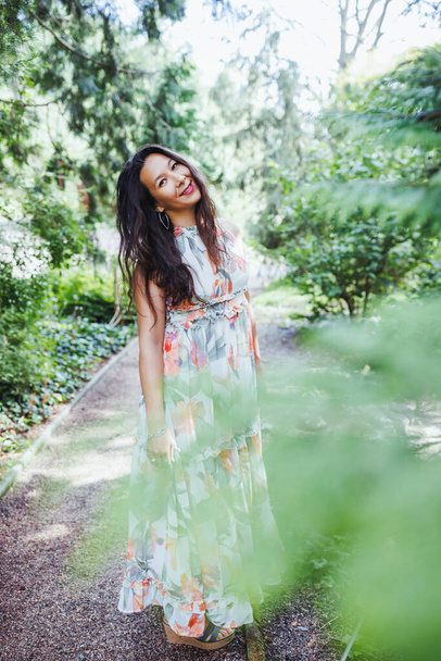 Beautiful happy mixed race Japanese woman in romantic floral maxi dress in summer park, smiling. Full body shot. Sunlight, copy space - Fotografie, Obrázek