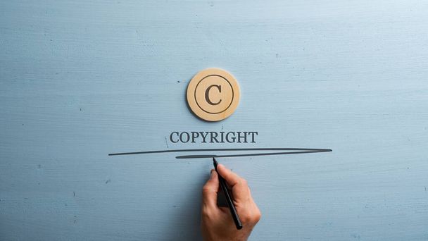 Circled letter C on a wooden cut circle with male hand writing a Copyright word under it. Over wooden blue background. - Fotoğraf, Görsel