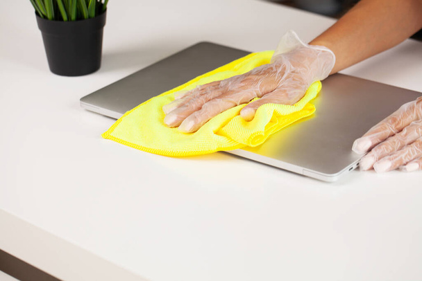 Een schoonmaker reinigt het kantoor door stof van een laptop af te vegen. - Foto, afbeelding
