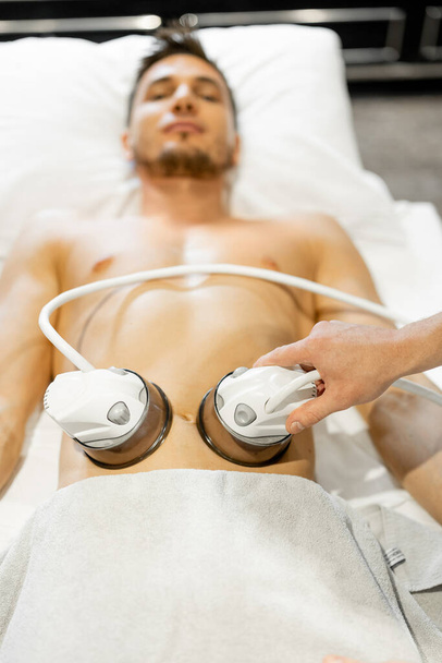 Man receiving vacuum roller massage on belly arrea at medical beauty centre. Lymphatic drainage massage procedure - Foto, imagen