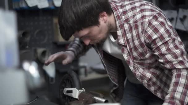 Handyman fija una rueda de un scooter sujetado en un clevis y la tuerce con una llave creciente en la tienda. Reparador utiliza una llave ajustable para reparar una parte de una bicicleta para niños en el taller. - Metraje, vídeo