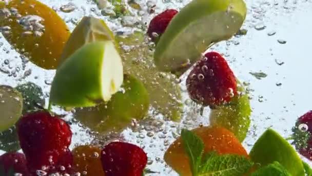 Κοντινό πλάνο κομμάτια φρούτων βυθισμένο καθαρό νερό σε λευκό φόντο. Ζουμερά βιολογικά φράουλα πορτοκάλι μήλο μέντα λεμόνι επιπλέουν με φυσαλίδες σε σούπερ αργή κίνηση. Νόστιμη τροφή βιταμινών για υγιεινή διατροφή. - Πλάνα, βίντεο