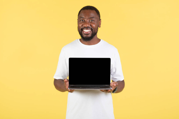 Happy African American Guy ukazuje notebook s prázdnou obrazovkou reklama webové stránky stojící s úsměvem na kameru přes žluté Studio na pozadí. E-Learning And Internet Technology. Mockup - Fotografie, Obrázek