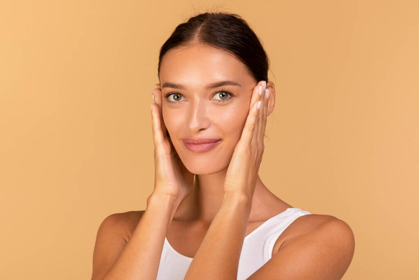 Essential beauty. Portrait of happy lady touching her smooth skin, looking at camera, enjoying result of beauty treatments over beige studio background - Foto, imagen