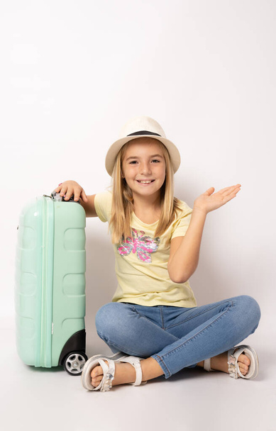 Lapsi tyttö olkihattu istuu lattialla matkalaukku valkoisella taustalla. Pieni tyttö haaveilee matka, seikkailu, loma. - Valokuva, kuva