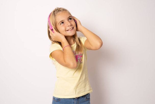 Photo portrait of little girl smiling touching headphones listening to music isolated on white background - Photo, Image