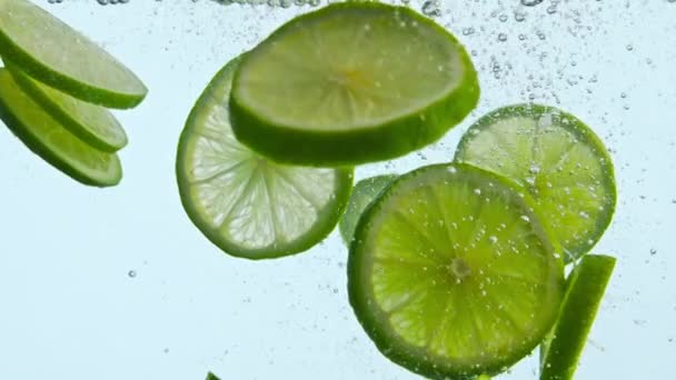 Φρέσκο πράσινο λάιμ κάτω από το νερό σε λευκό φόντο κοντά. Ωριμότητα ξινή εσπεριδοειδών που επιπλέουν με φυσαλίδες σε διαφανές νερό σούπερ αργή κίνηση. Βιταμίνη υγιή φρούτα για δροσιστικό ποτό. Έννοια διατροφής. - Πλάνα, βίντεο