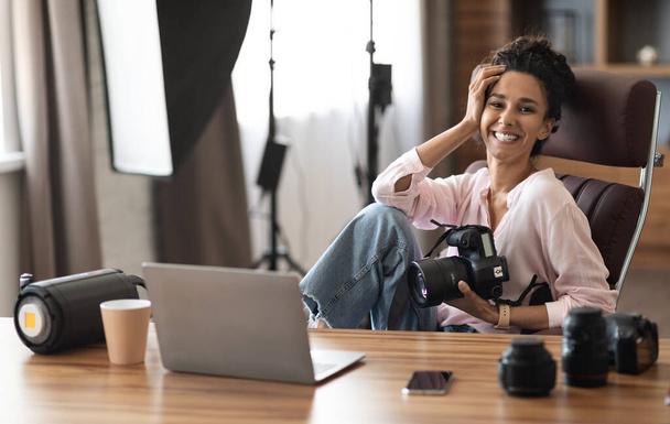 Happy pretty millennail vrouw fotograaf werken thuis kantoor, zitten aan een bureau met moderne laptop op, met professionele camera, het drinken van koffie, het controleren van foto 's, kopiëren ruimte - Foto, afbeelding