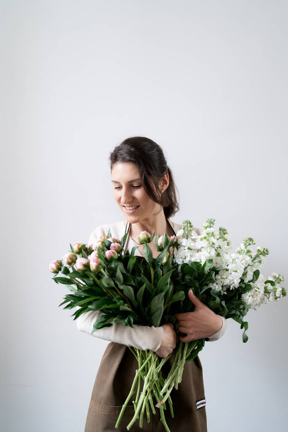 WOMAN florist EMBRACING a bunch of white and pink flowers on white background indoors - Фото, изображение