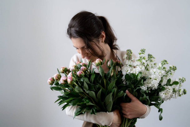 WOMAN florist EMBRACING a bunch of white and pink flowers on white background indoors - Fotoğraf, Görsel