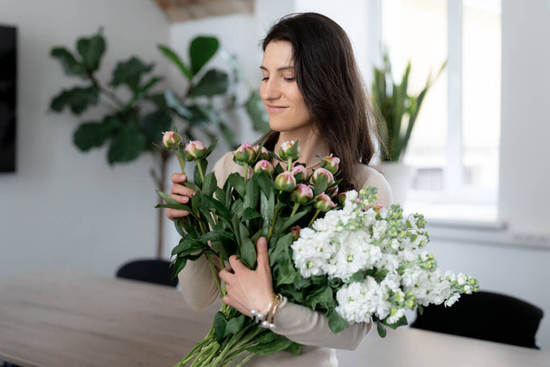 Positive woman holding a huge bouquet of flowers in her office. Birthday present smile. - Foto, Bild
