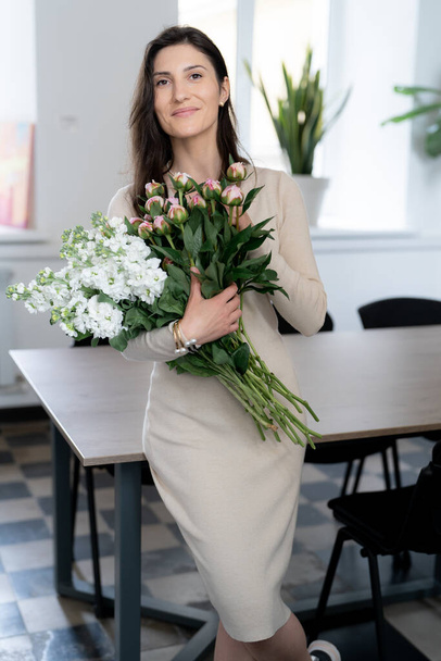 Mujer positiva sosteniendo un enorme ramo de flores en su oficina. Cumpleaños presente sonrisa. - Foto, Imagen