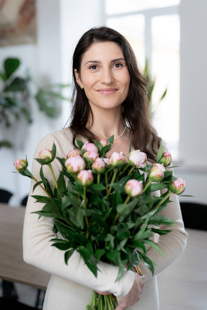 積極的な女性は彼女のオフィスで花の巨大な花束を保持します。誕生日プレゼント笑顔. - 写真・画像