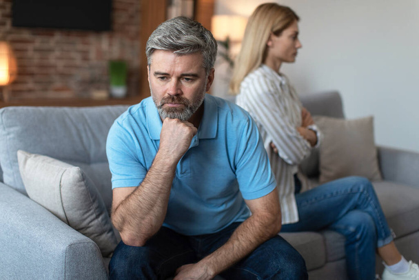Unhappy middle aged european man ignores offended lady after quarrel in living room interior, copy space. Family emotions, relationship problems, scandal and stress at home during covid-19 pandemic - Photo, Image