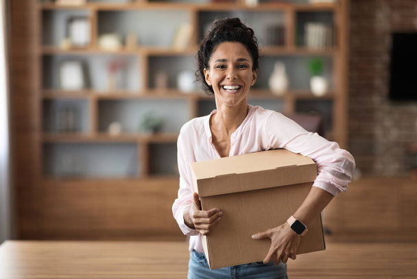 Happy pretty young woman in casual embracing box with something and smiling at camera, home interior, making order on Internet with delivery, copy space. Delivery service, shipment concept - Photo, Image