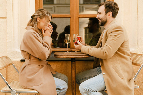 White man proposing to his excited girlfriend in cafe outdoors - Fotoğraf, Görsel