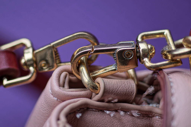 yellow metal latch with a ring on the strap of a leather pink bag on a purple background - Фото, зображення