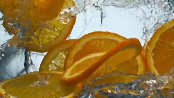Jasné plátky chutné pomeranče cákající průhlednou vodu v super zpomaleném filmu zblízka. Vitamin čerstvé citrusy padající čiré kapaliny na bílém pozadí. Lahodná tropická přísada pro limonádu. - Záběry, video