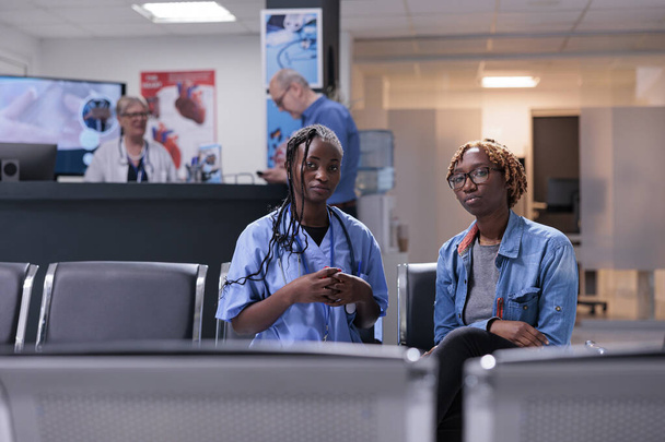 Ritratto di persone afro-americane sedute nella hall della sala d'attesa e nel centro sanitario, che fanno visite di controllo presso la struttura. Specialista e paziente che ha un appuntamento medico per il supporto sanitario. - Foto, immagini