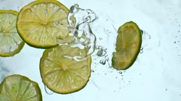 Verse limoenschijfjes vallen helder water in super slow motion close-up. Heldere sappige stukken zure citrus drijvende transparante vloeistof op witte achtergrond. Vitamine smakelijk fruit voor cocktail limonade. - Video