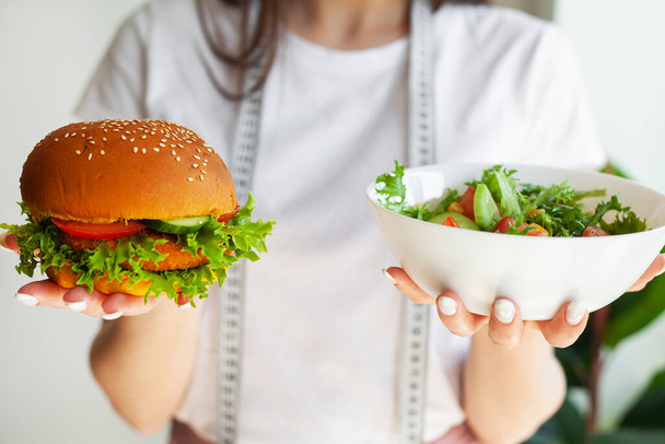 Žena se rozhodne jíst hamburger nebo čerstvý salát v kuchyni. - Fotografie, Obrázek