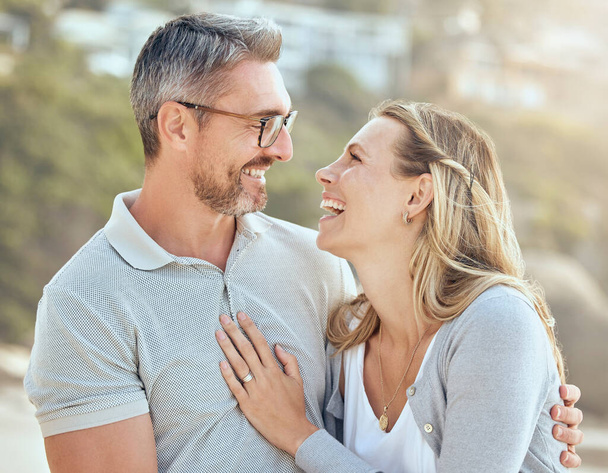 Gelukkig en liefdevol volwassen blanke echtpaar genieten van een romantische date op het strand samen op een zonnige dag. Vrolijke aanhankelijke man en vrouw hechting op vakantie buiten. - Foto, afbeelding