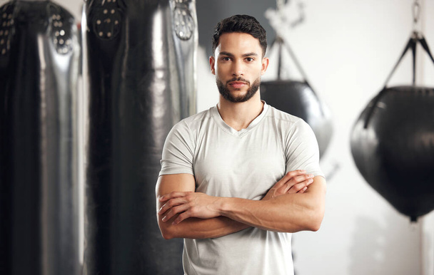 Portrait of one serious young hispanic man standing with his arms crossed ready for exercise in a gym. Muscular mixed race instructor looking focused and motivated for training workout in a fitness c. - Photo, Image