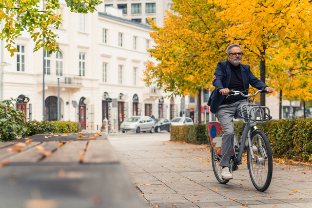 Fall outdoor activities. Full-length shot of middle-aged caucasian bearded man in business casual clothing riding a rented bike. Autumn in the city. High quality photo - Photo, Image