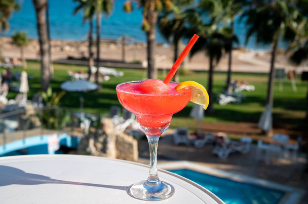 Colorato congelato rosa Fragola daiquiri cocktail drink servito in vetro al bar della piscina con vista sulla piscina blu, mare e palme, relax e vacanze al mare - Foto, immagini