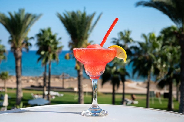 Barevné mražené růžové Jahodové daiquiri koktejlové nápoje podávané ve skle v venkovní kavárně s výhledem na modré moře a palmy, relaxaci a dovolenou na moři - Fotografie, Obrázek