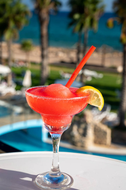 Барвистий заморожений рожевий коктейльний напій з полуниці, який подають у склянці у відкритому кафе з видом на блакитний басейн, море та пальми, відпочинок та відпочинок на морі
 - Фото, зображення