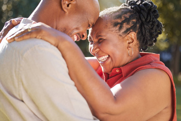 Happy affectionate mature african american couple sharing an intimate moment outside at the park during summer. In love seniors smiling and embracing while spending quality time together outdoors. - Photo, image