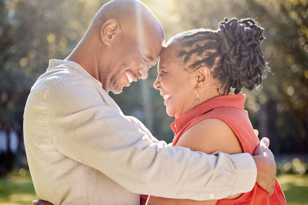 Gelukkig liefdevol volwassen Afrikaans-Amerikaans echtpaar delen een intiem moment buiten in het park in de zomer. In de liefde senioren glimlachen en omhelzen terwijl het doorbrengen van kwaliteitstijd samen buiten. - Foto, afbeelding
