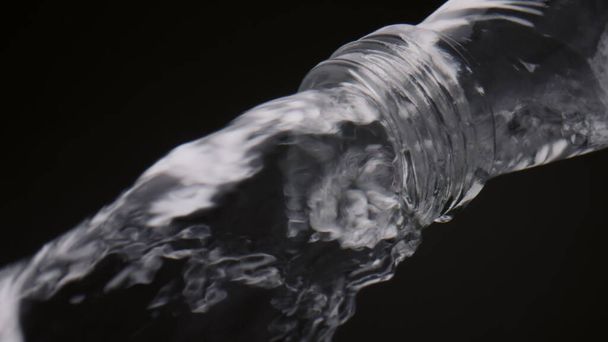 Água mineral derramando gargalo garrafa em movimento super lento de perto. Fluxo rápido de líquido transparente que flui para baixo do recipiente de vidro no fundo preto. Bebida orgânica fresca para uma vida saudável de energia. - Foto, Imagem