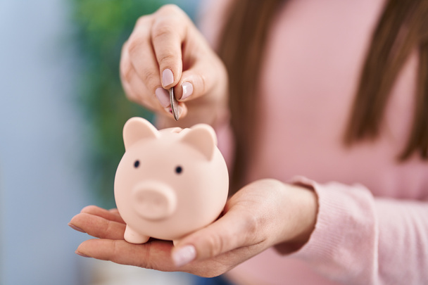Young woman inserting coin on piggy bank at home - Photo, Image