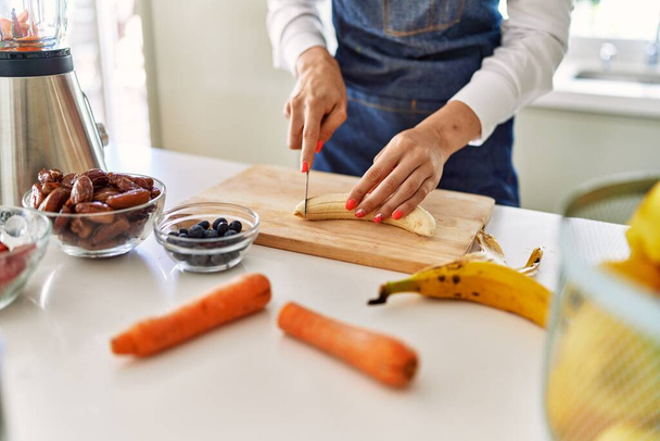 Young blonde woman cutting banana at kitchen - Фото, зображення