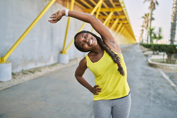 Mujer afroamericana usando ropa deportiva estirando el brazo en la calle - Foto, imagen