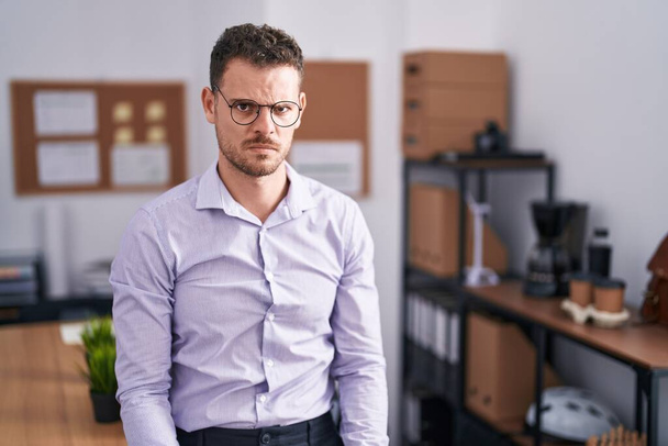 Jonge Spaanse man op kantoor sceptisch en nerveus, fronsend van streek vanwege het probleem. negatieve persoon.  - Foto, afbeelding