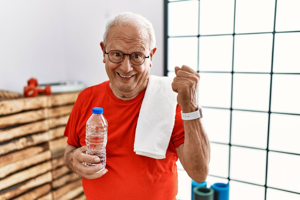 Starszy mężczyzna w odzieży sportowej i ręczniku na siłowni bardzo szczęśliwy i podekscytowany wykonując gest zwycięzcy z podniesionymi ramionami, uśmiechnięty i krzyczący o sukces. koncepcja uroczystości.  - Zdjęcie, obraz