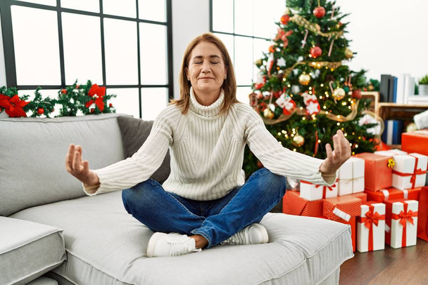 Kaukasische Frau mittleren Alters macht Yoga-Übungen zu Hause am Weihnachtsbaum - Foto, Bild