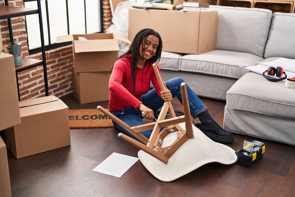 African american woman smiling confident repair chair at new home - Photo, Image