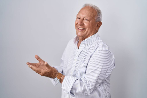 Senior mies harmaat hiukset seisoo eristetty tausta osoittaa sivuun kädet auki kämmenet näyttää kopioi tilaa, esittää mainos hymyillen innoissaan onnellinen  - Valokuva, kuva