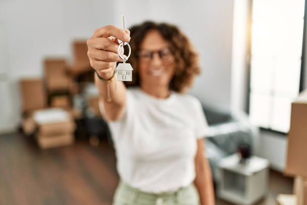 Mujer hispana de mediana edad sonriendo feliz sosteniendo la llave de la casa en un nuevo hogar - Foto, Imagen