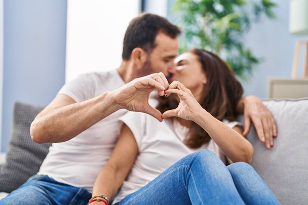 Middle age man and woman couple doing heart gesture with hands sitting on sofa at home - Foto, immagini