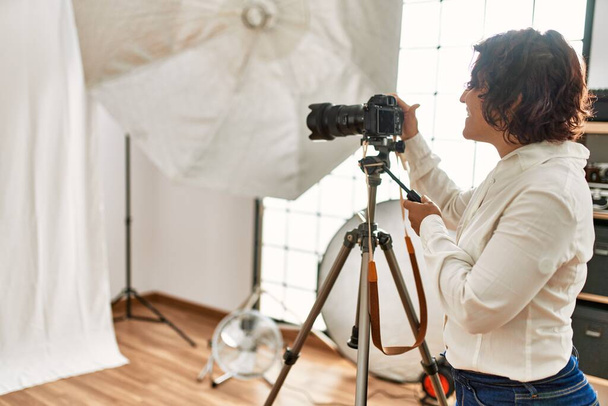 Genç İspanyol fotoğrafçı kadın fotoğraf stüdyosunda kamerayla mutlu bir şekilde gülümsüyor.. - Fotoğraf, Görsel