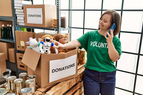 Брюнетка с синдромом Дауна стоящая коробка говорит по телефону на стенде пожертвований - Фото, изображение