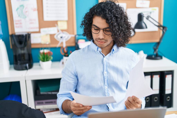 Молодий латинський працівник бізнесу використовує документ для читання ноутбуків в офісі
 - Фото, зображення