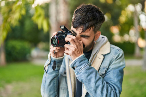 Young hispanic man using professional camera at park - 写真・画像