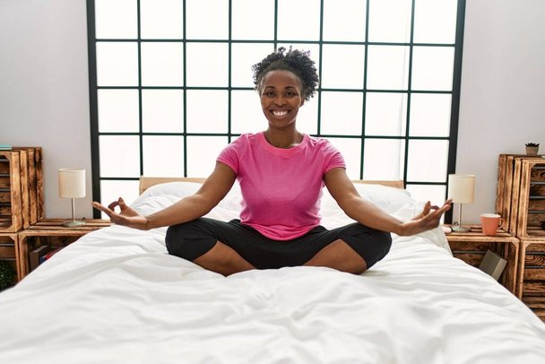 Mujer afroamericana haciendo ejercicio de yoga sentada en la cama en el dormitorio - Foto, imagen